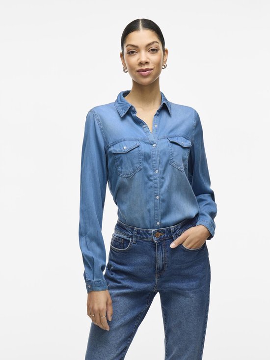 Model draagt een blauwe denim blouse van VILA met lange mouwen, twee opgestikte borstzakken en drukknoopsluiting. Zichtbaar van voren.