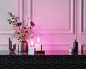 Een decoratieve vaas met bloemen en twee lampen op witte sokkels, badend in roze licht.