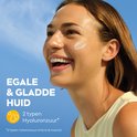 Vrolijke jonge vrouw lacht naar de camera met een witte crème op haar wang. Tekst: "EGALE & GLADDE HUID", "2 typen Hyaluronzuur".