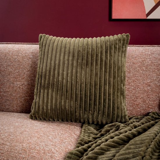 Olijfgroen ribfluwelen kussen met verticale ribbels op een roze bank met plaid.