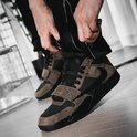 Bruine en zwarte lage sneakers met klittenbandsluiting, gedragen door iemand die zijn broek sluit.