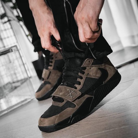 Bruine en zwarte lage sneakers met klittenbandsluiting, gedragen door iemand die zijn broek sluit.
