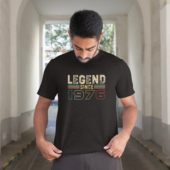 Man met donker haar in zwart T-shirt met de tekst "LEGEND SINCE 1976" in retrokleuren.