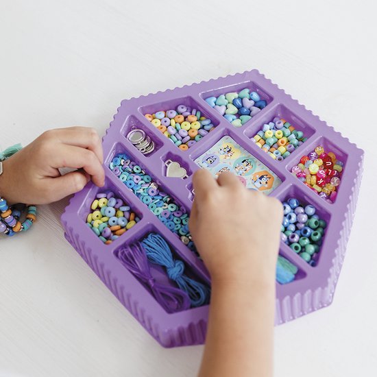 Paarse kralenset met veel gekleurde kralen, gevuld met touw, bedels en stickers. Kinderhanden maken armbanden.