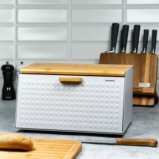Boîte à pain blanche en métal avec motif diamant et couvercle en bois. À côté d'une planche à pain avec du pain.