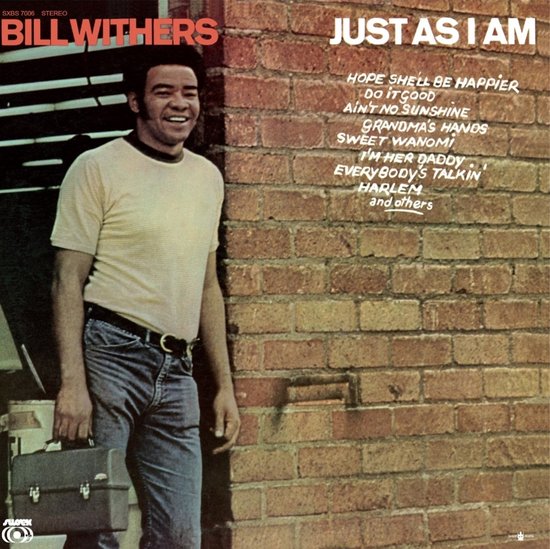 Bill Withers, 'Just As I Am' elpeehoes. Man draagt lichtgekleurd T-shirt en spijkerbroek, houdt een koffer vast, tegen een bakstenen muur.