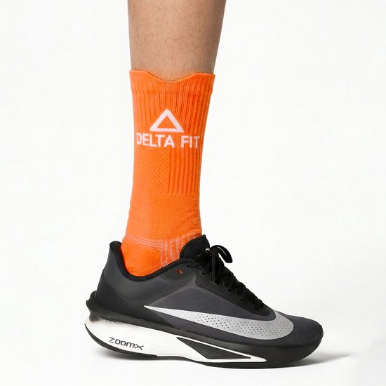 Oranje compressiesokken met witte 'DELTA FIT' opdruk, gedragen met een zwarte hardloopschoen.