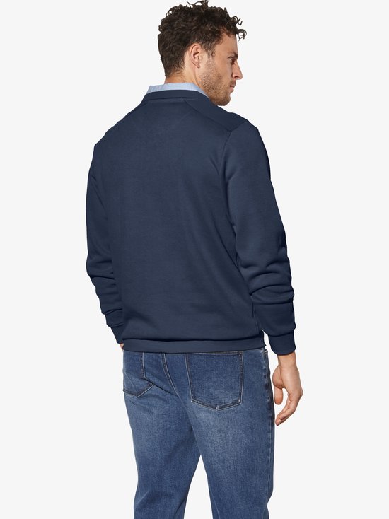 Donkerblauwe sweater met hoge hals, gedragen door een man met spijkerbroek.