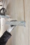 Hand met grijze werkhandschoen bevestigt een metalen anker aan een betonnen muur met een hamer.