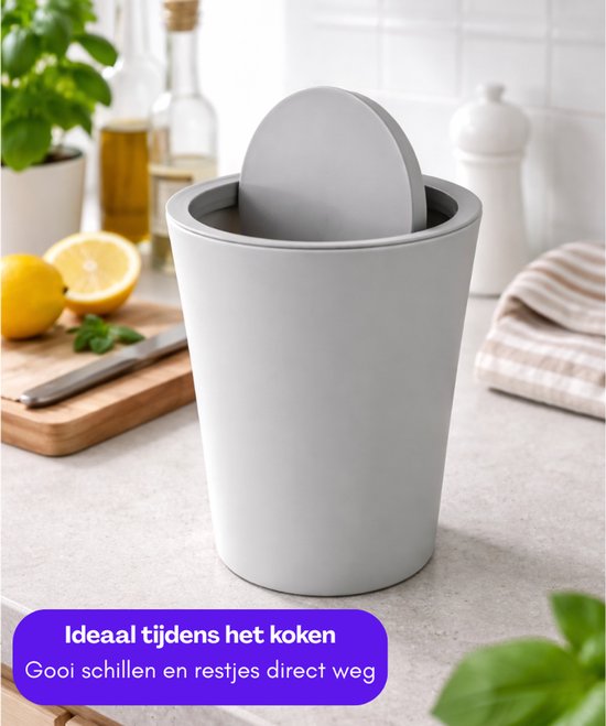 Grijze miniprullenbak met deksel op een aanrecht, met citroenen en kruiden. Tekst: 'Ideaal tijdens het koken. Gooi schillen en restjes direct weg'.