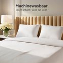 Twee witte CozySense kussens op een opgemaakt bed met beige hoofdbord. 'Machinewasbaar'.