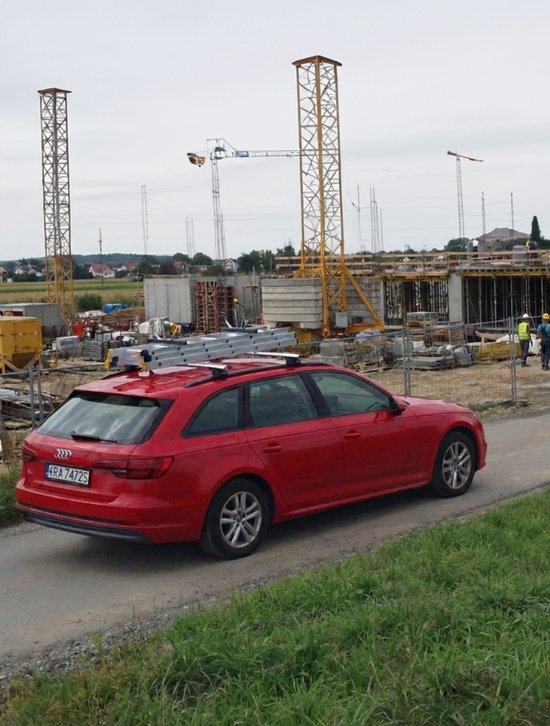 Rode Audi stationwagon met ladderdrager op een bouwplaats.