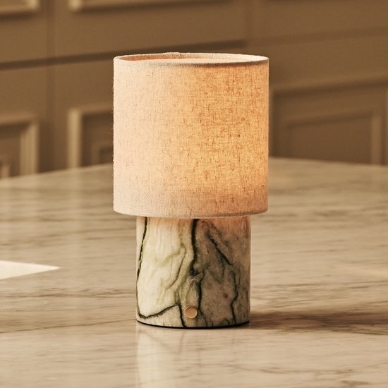 Tafellamp met groene marmeren voet en beige linnen kap op een marmeren tafel.