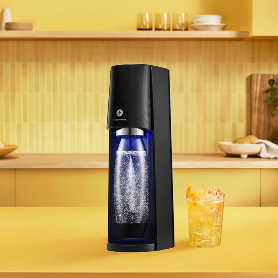 Zwarte SodaStream E-Terra met bruisende fles en glas bruiswater met sinaasappel.