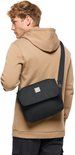 Model met blonde haren draagt een zwarte Vaude schoudertas over zijn schouder, gedragen over een beige hoodie.