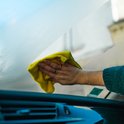 Een gele microvezeldoek veegt een beslagen autoruit schoon. De hand draagt ringen.