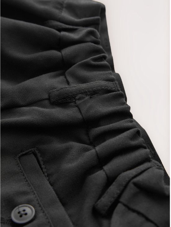 Gedetailleerde elastische tailleband van een zwarte broek met knopen.