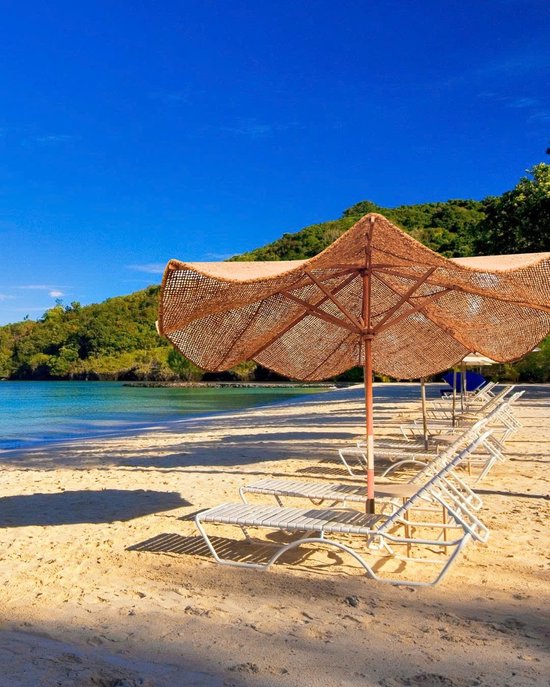 Bruine kokos parasol met houten frame staat op een zandstrand, met ligstoelen en de oceaan op de achtergrond.