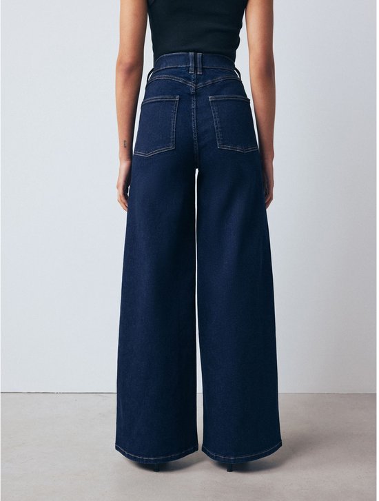 Donkerblauwe, wijde spijkerbroek met hoge taille, gedragen door een model van achteren gezien.
