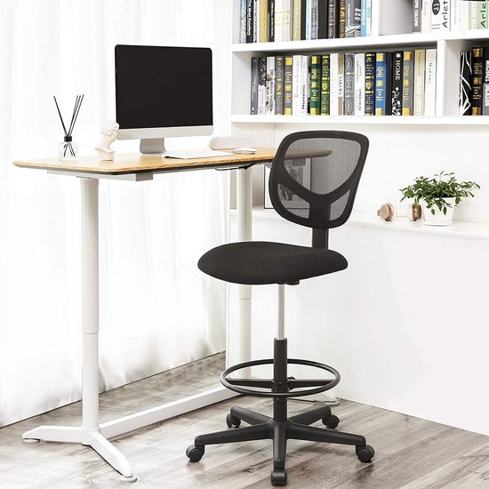 Zwarte bureaustoel met mesh rugleuning naast een sta-bureau, met boekenplanken op de achtergrond.