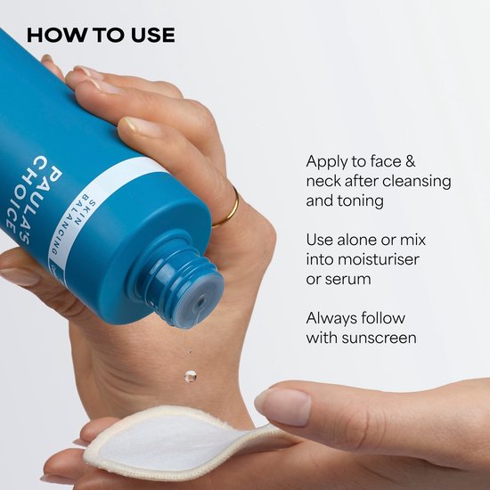 Hand met gouden ring houdt Paula's Choice Skin Balancing fles boven een wattenschijfje, een druppel vloeistof valt.