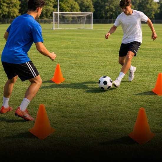 Twee mannen trainen voetbal op een grasveld met oranje pionnen.
