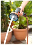 Een hand houdt een grijze Gardena sproeikop vast, terwijl een krachtige waterstraal eruit komt.
