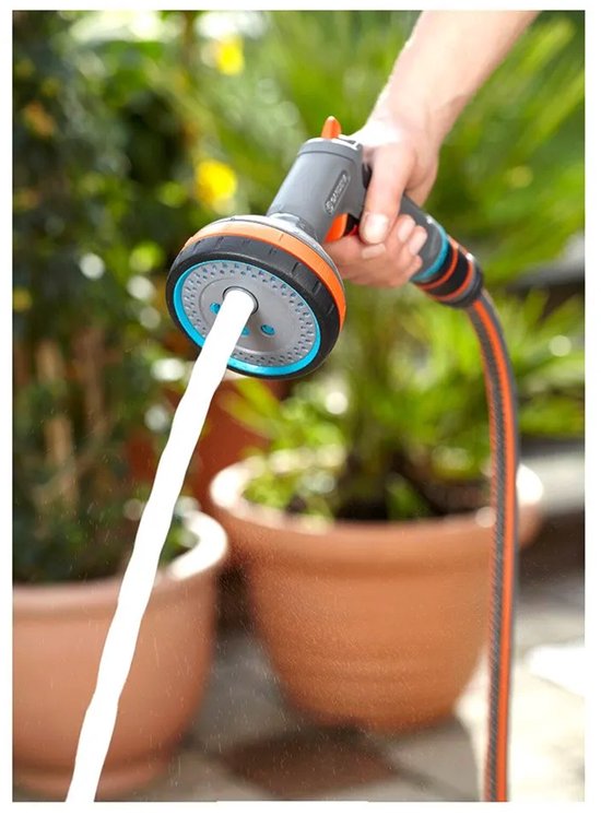 Een hand houdt een grijze Gardena sproeikop vast, terwijl een krachtige waterstraal eruit komt.