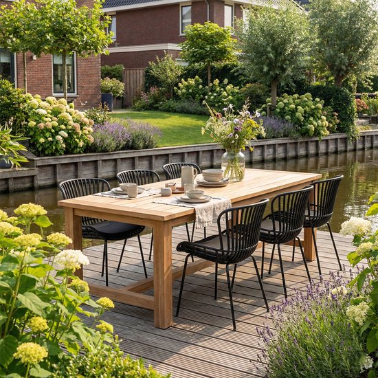 Tafel en zes zwarte tuinstoelen met open rugleuningen aan een houten vlonder bij een tuin met water.
