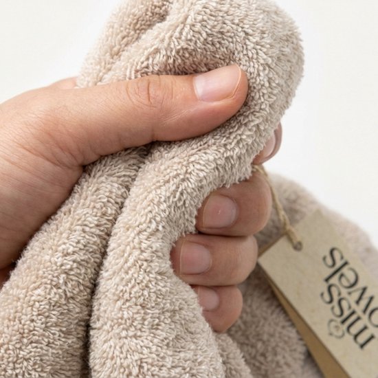 Hand pakt een zandkleurige, zachte badhanddoek met een bruin label.
