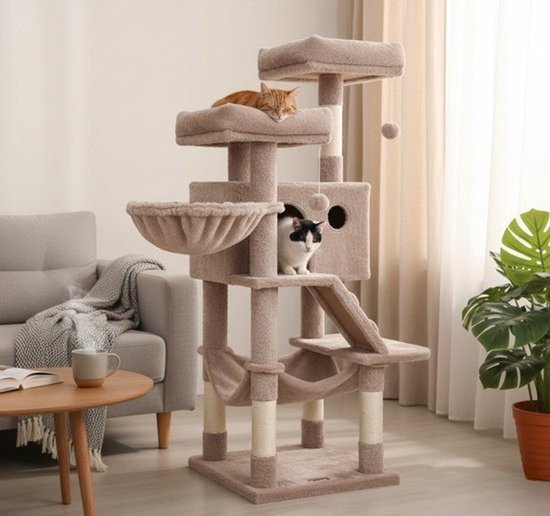 Luxe beige kattenboom met hangmat, mand en speelgoed. Een rode kat slaapt bovenop, een zwart-witte kat kijkt uit een holletje.