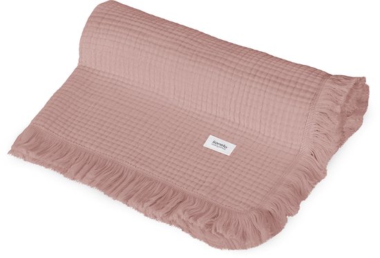 Lichtroze mousseline deken opgerold met zichtbare franjes en een label.