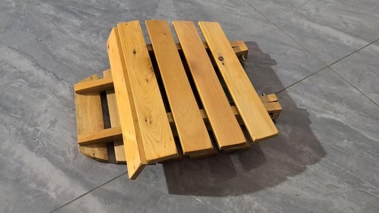 Houten opklapbare kruk van bovenaf gezien, met zitting en rugleuning in houtkleur, op een grijze tegelvloer.