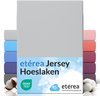 Un drap-housse gris clair empilé avec un arc-en-ciel de draps-housses colorés derrière. "Drap-housse jersey etérea"