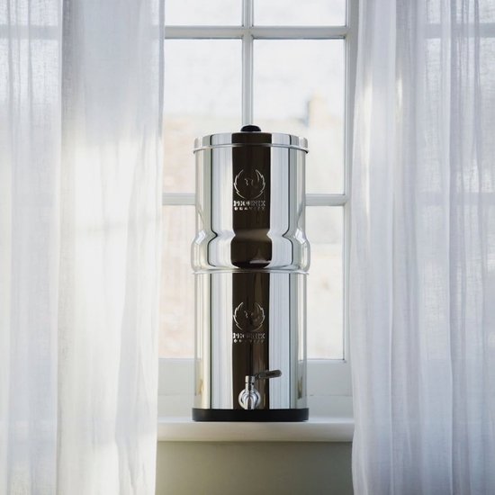 Phoenix Gravity 6 liter RVS waterfilter op een vensterbank tussen witte vitrage