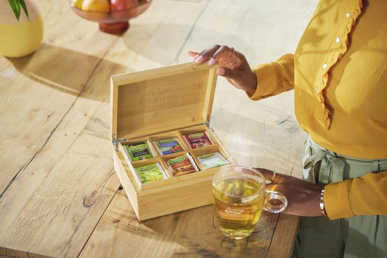Een houten theedoos van Pickwick met 6 verschillende theesmaken, geopend met een vrouw in een mosterdgele blouse.