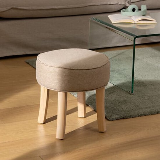 Beige stoffen krukje met houten poten in een woonkamer.