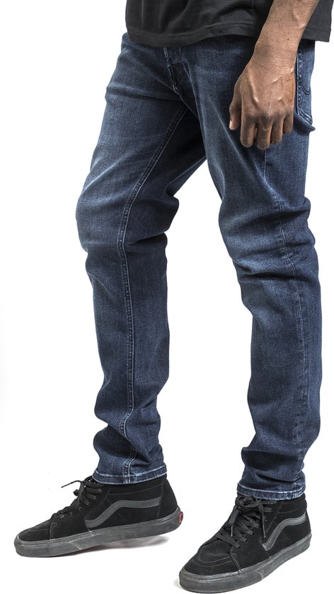Zij-aanzicht van een man die een blauwe spijkerbroek en zwarte sneakers draagt.