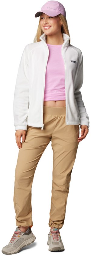 Een staande blonde vrouw in een witte fleece trui, roze crop top en beige joggingbroek.