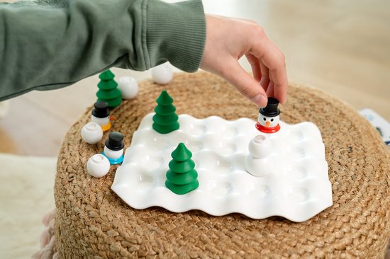 Hand legt sneeuwpop op spelbord "Snow Problem" met bomen en witte ballen.