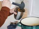 Mains remplissant un lunchpot isotherme argenté avec de la soupe à l'aide d'une louche.