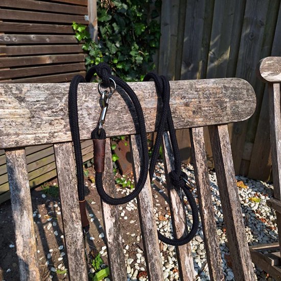 Zwarte, dikke katoenen hondenriem met bruin lederen detail en metalen karabijnhaak, rustend op een houten bankje.