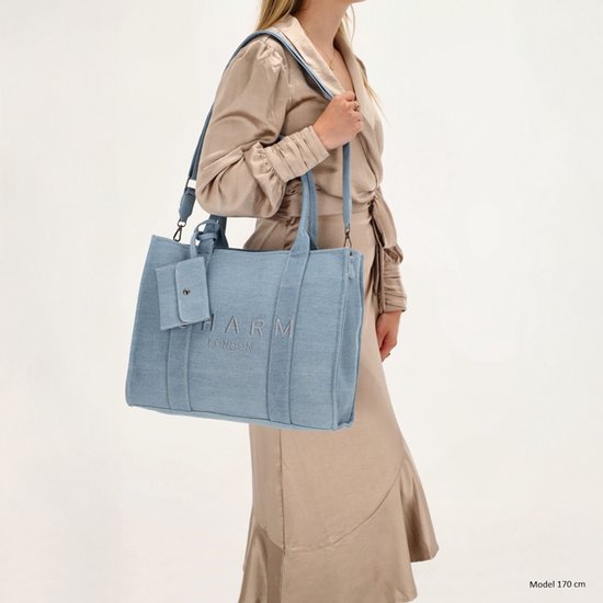 Model van 170 cm draagt een lichtblauwe denim shopper met 'CHARM LONDON' opdruk en een klepje.