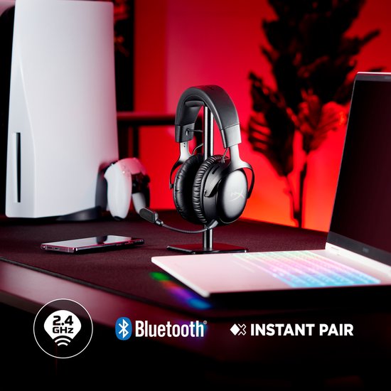 Zwarte HyperX Cloud III S Wireless gaming headset op een standaard, naast een PlayStation 5, controller en laptop.
