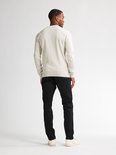 Man met beige trui en zwarte jeans, van achteren gezien.