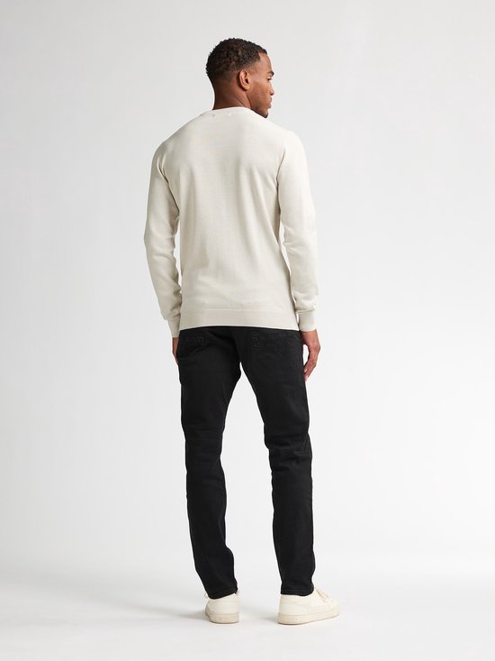 Man met beige trui en zwarte jeans, van achteren gezien.
