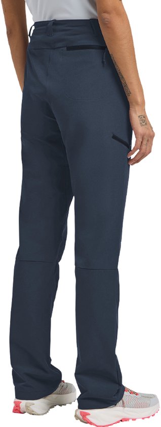 Vrouw in donkerblauwe outdoorbroek, zicht op achterkant, met ritszakken en sneakers.