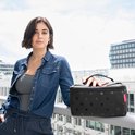 Vrouw met sproeten, gekleed in een spijkerblouse, houdt een zwarte toilettas met stippen vast.