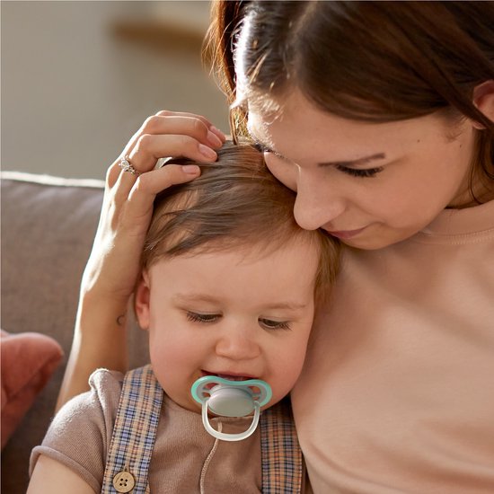 Vrouw met baby, die een speen met een lichtblauwe rand draagt. Baby draagt een tuinbroek.