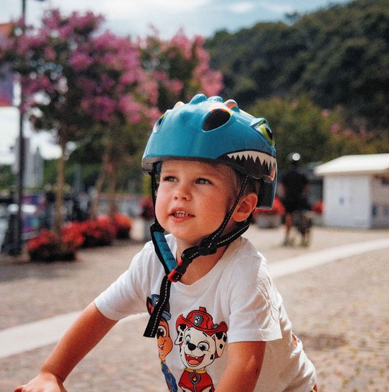 Lichtgroene kinderfietshelm met dinosaurusprint, drakenogen, scherpe tanden en gele accenten. Een jongen draagt de helm.